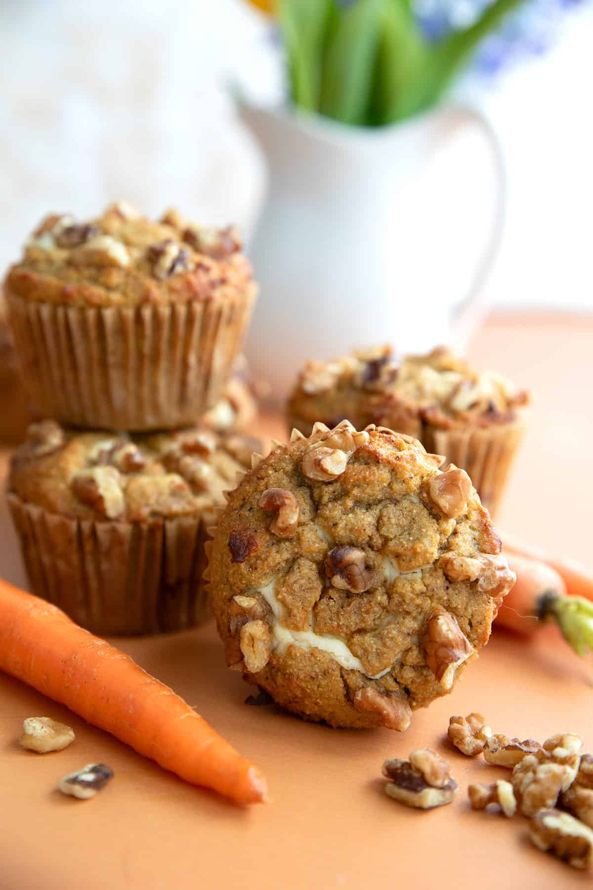 Keto Carrot Muffins piled up on a table top with a vase of spring flowers in the background.