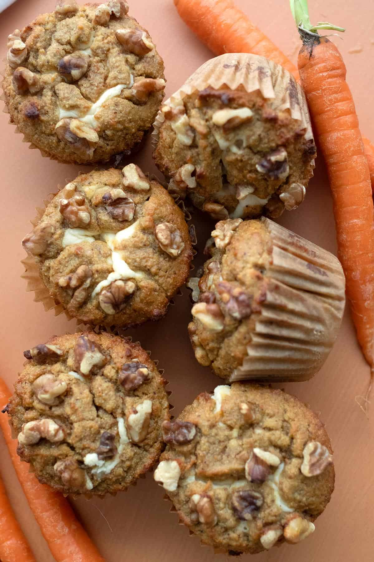 Top down image of keto carrot cake muffins on an orange tabletop with carrots pile around them.