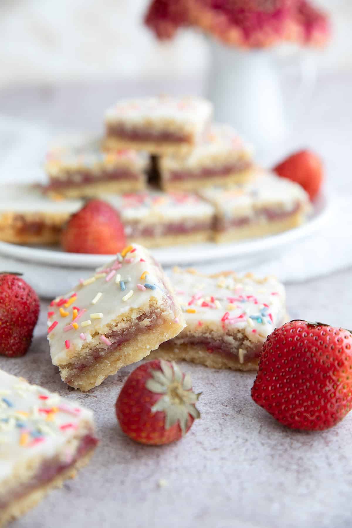 Two keto pop tart bars on a concrete table with fresh strawberries around it.