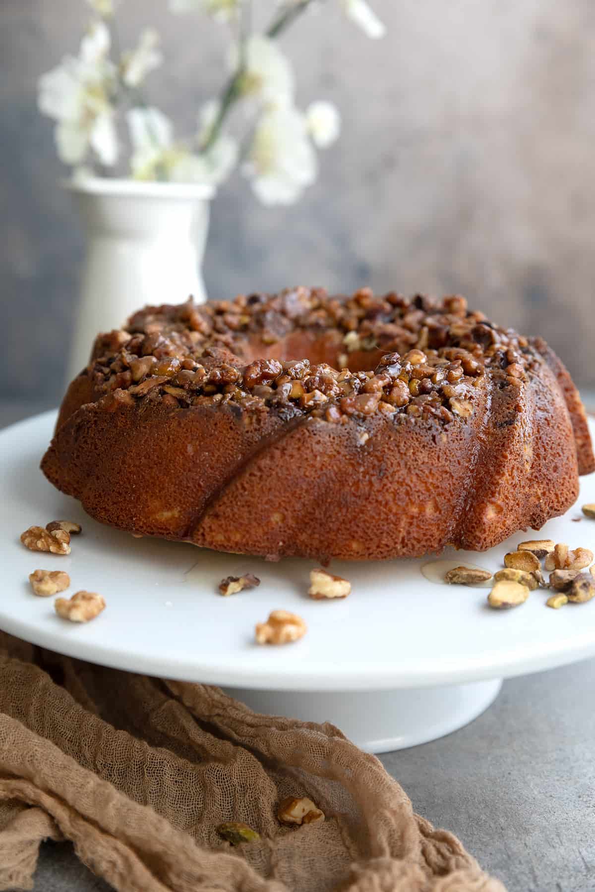 Keto Baklava Cake on a white cake stand with chopped nuts all around.
