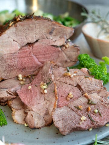 Sliced lamb roast on a grey plate with parsley.