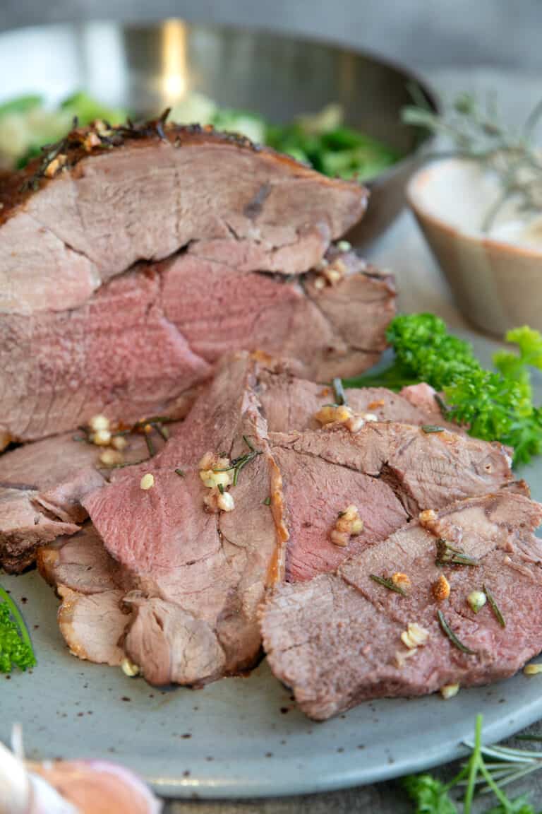 Sliced lamb roast on a grey plate with parsley.