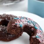 Two keto chocolate donuts on a white plate with one broken open to show the inside