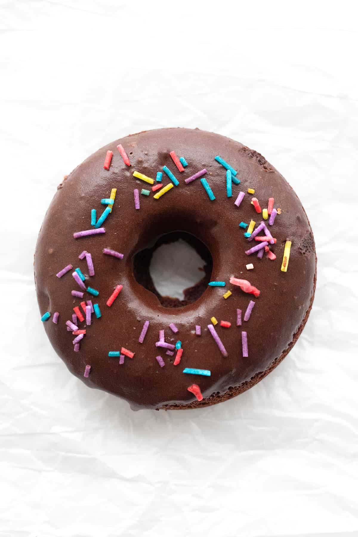 Top down image of a keto chocolate donut with sprinkles on a white background.