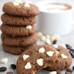 Two Keto Cappuccino Cookies in front of a stack of more cookies, with white chocolate chips and espresso beans strewn around.