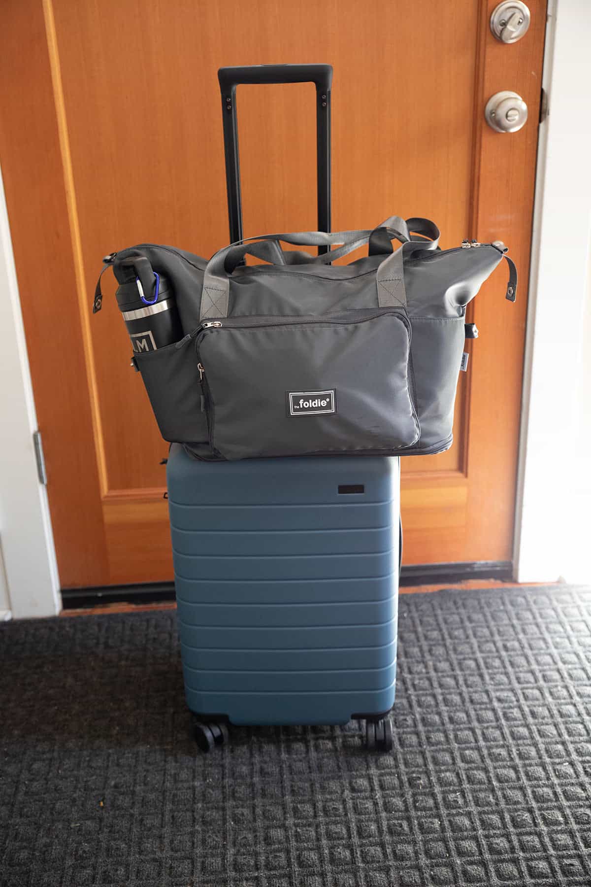 Gray expandable travel tote bag on top of carry-on suitcase. 