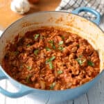 A small blue dutch oven filled with turkey ragu on a white table.