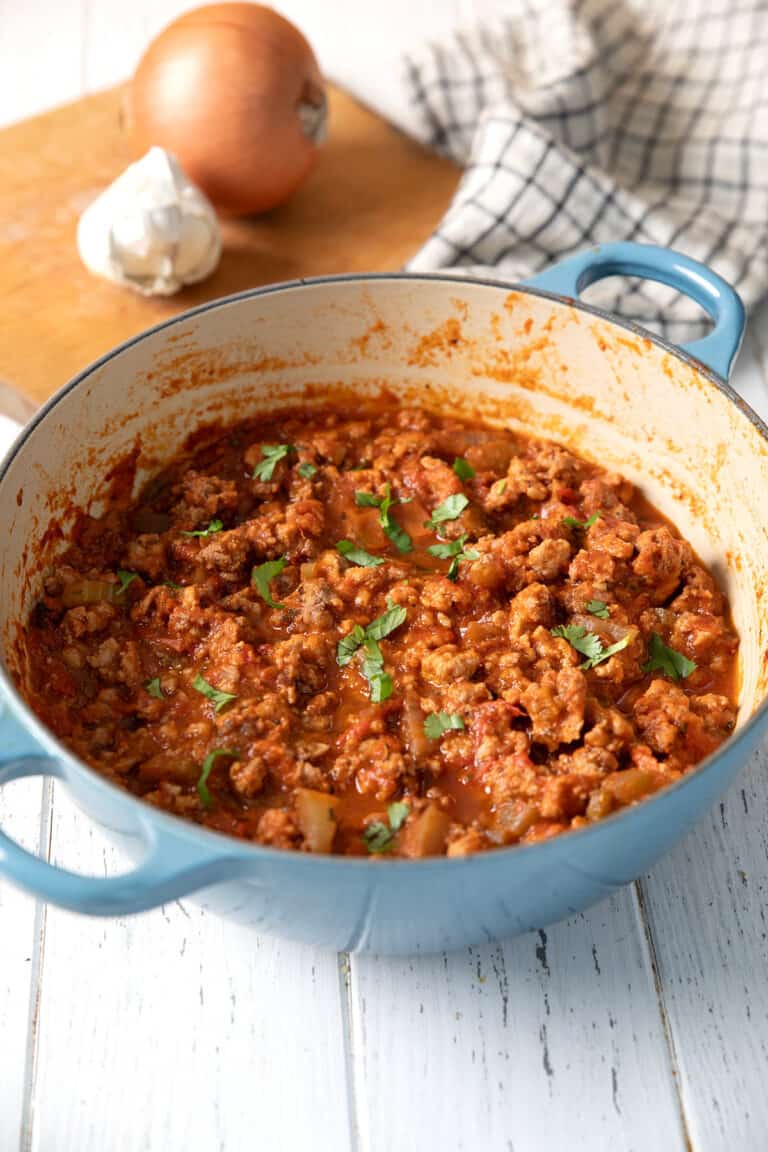 A small blue dutch oven filled with turkey ragu on a white table.