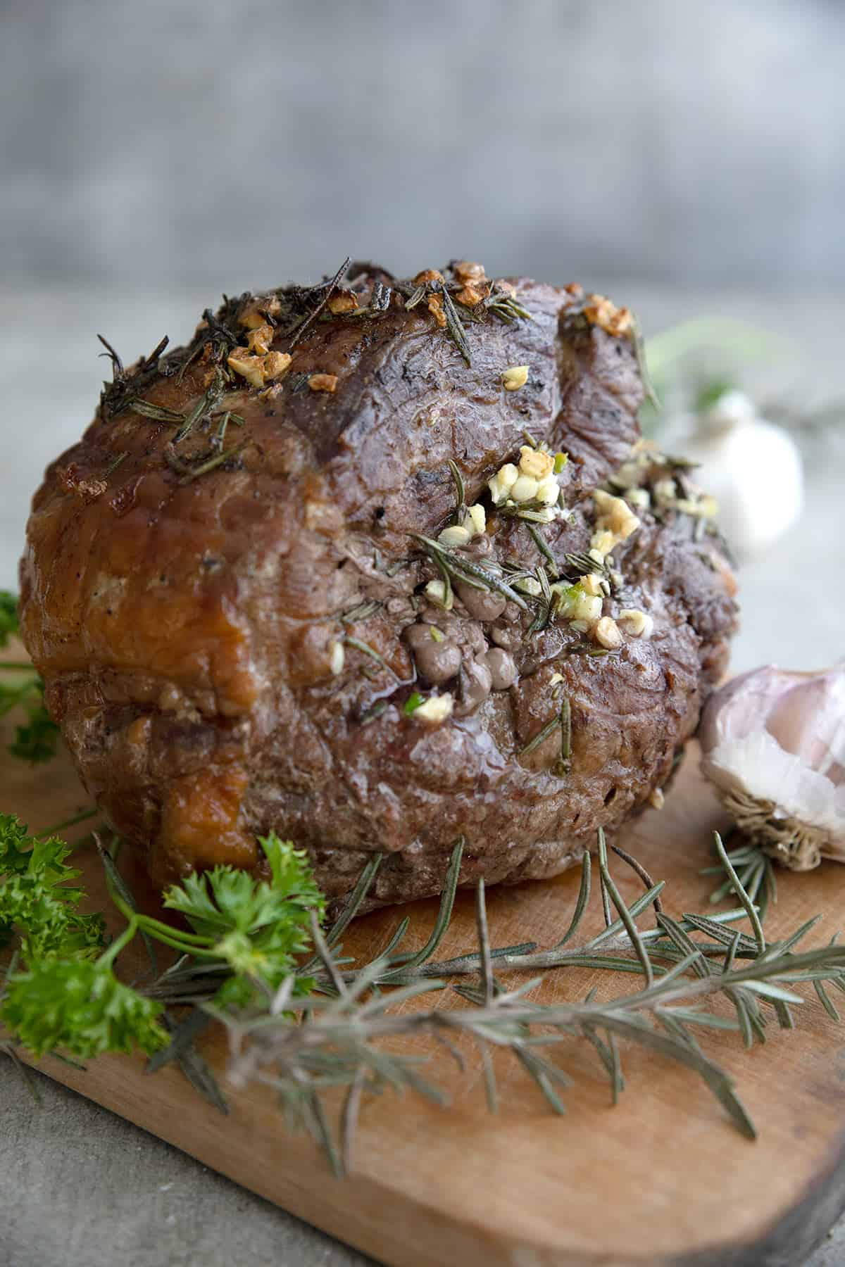 A leg of lamb cooked in an instant pot on a cutting board with garlic, rosemary and parsley.