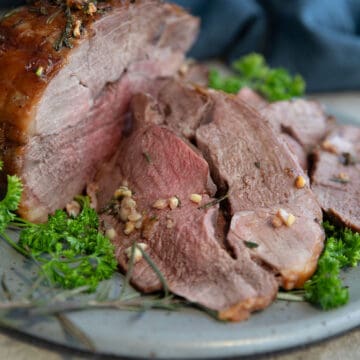 Sliced leg of lamb on a gray plate on a concrete table.