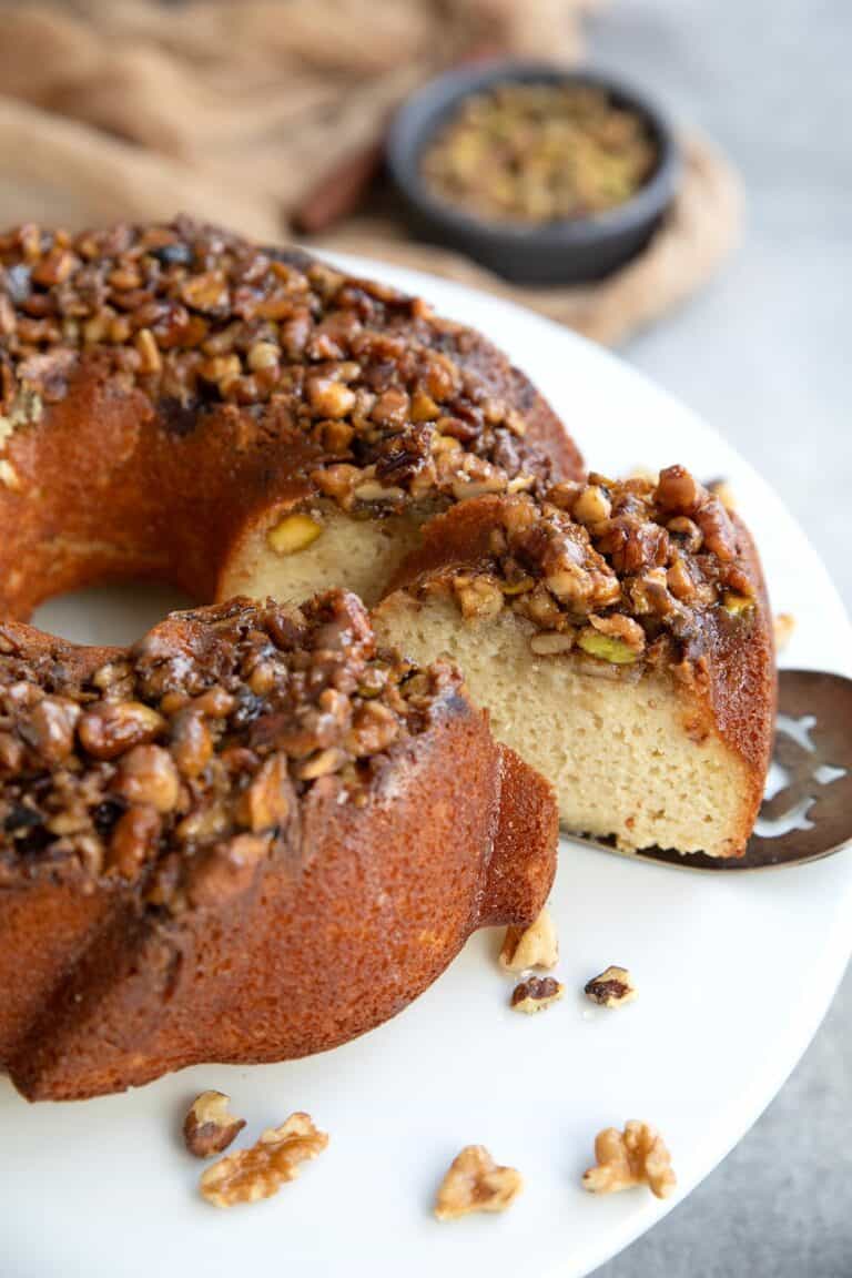 A slice of Baklava Bundt Cake being pulled away from the rest of the cake on a silver server.