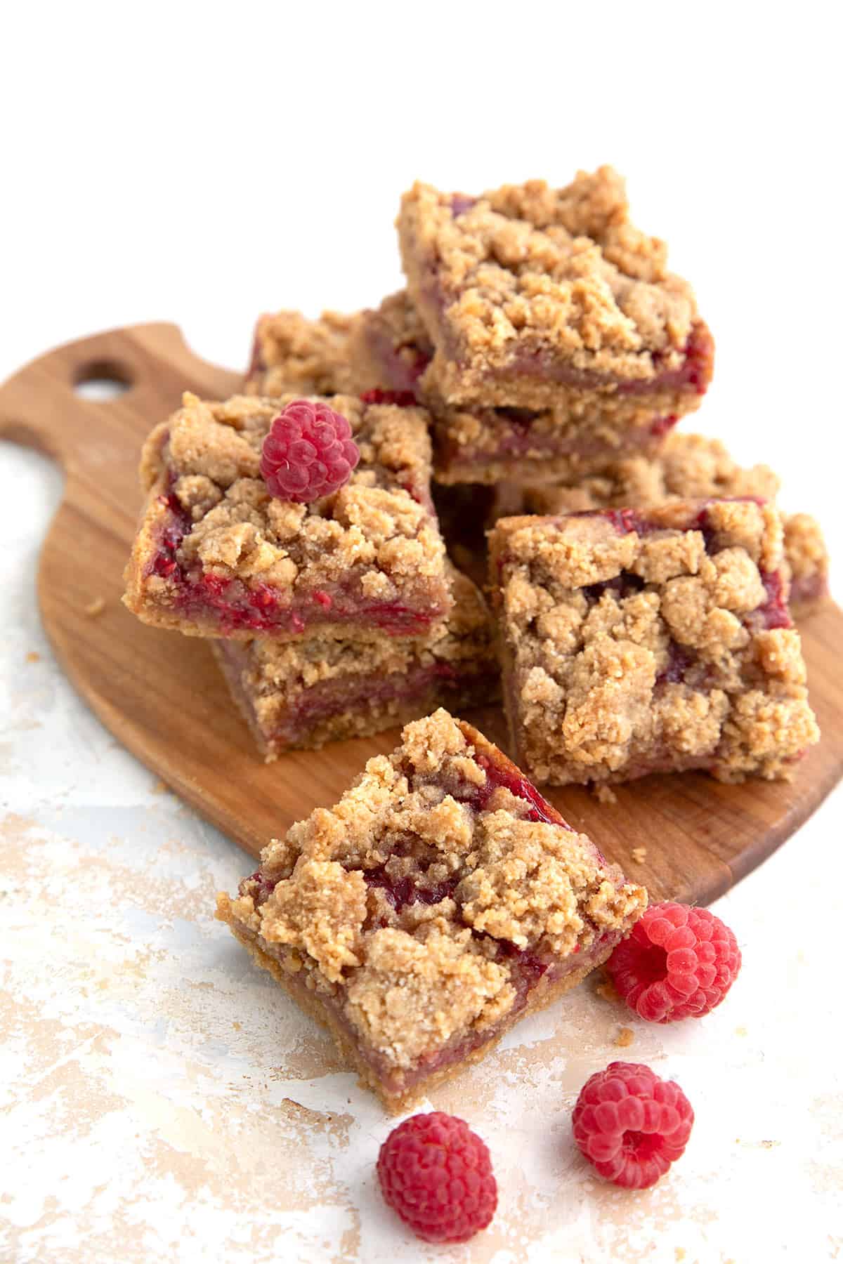 Peanut Butter and Jelly Bars on a wooden cutting board with fresh raspberries around it.