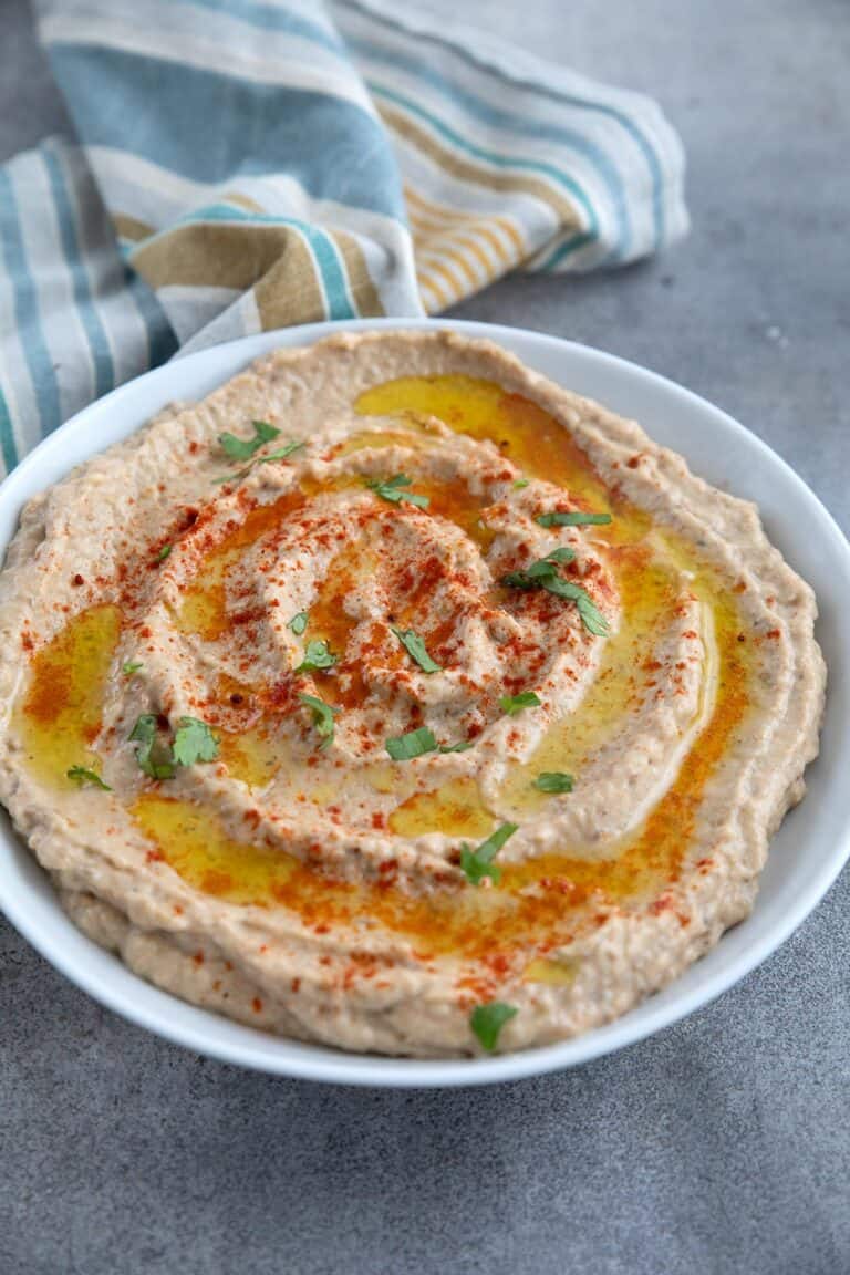 Creamy roasted eggplant dip in a white bowl on a concrete table, with a striped napkin in the background.