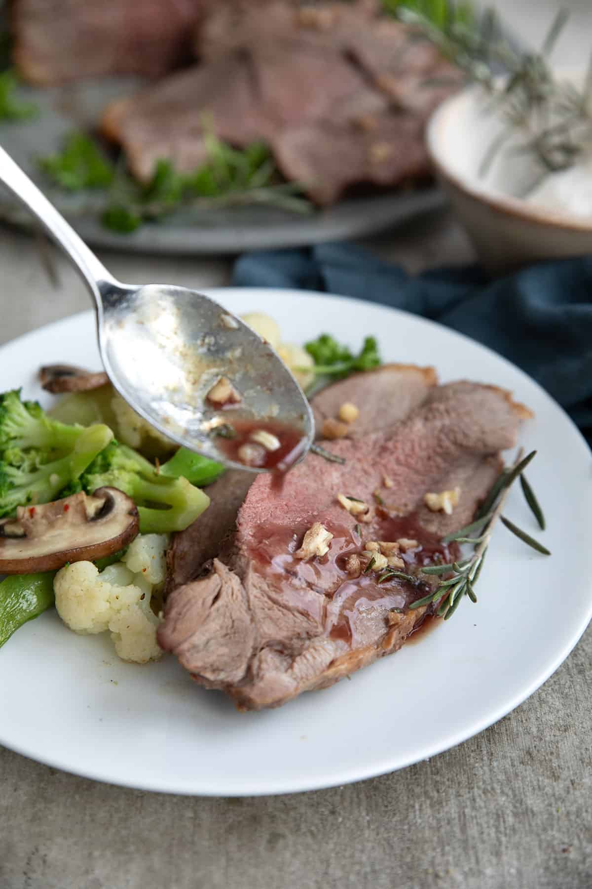 A spoon drizzling juices over sliced leg of lamb.