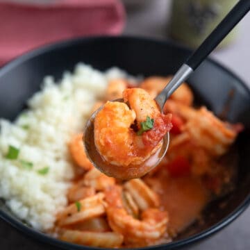 Close up shot of shrimp being lifted above a bowl of Shrimp Creole on a spoon.