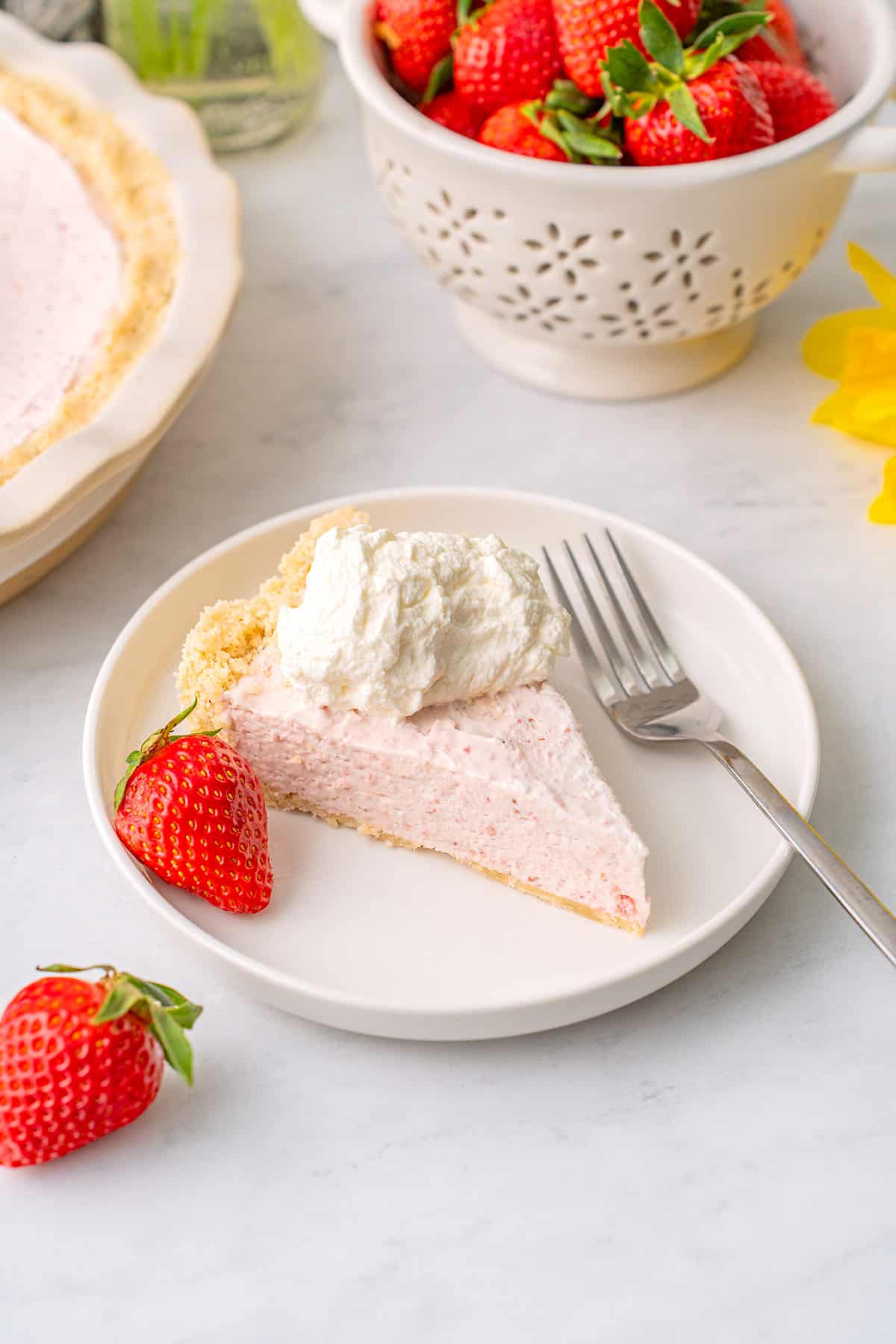 A slice of Keto Strawberry Pie on a white plate with strawberries and whipped cream.