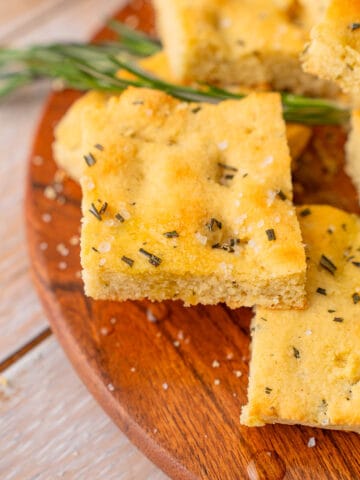 Squares of keto focaccia bread on a wooden plate with rosemary.