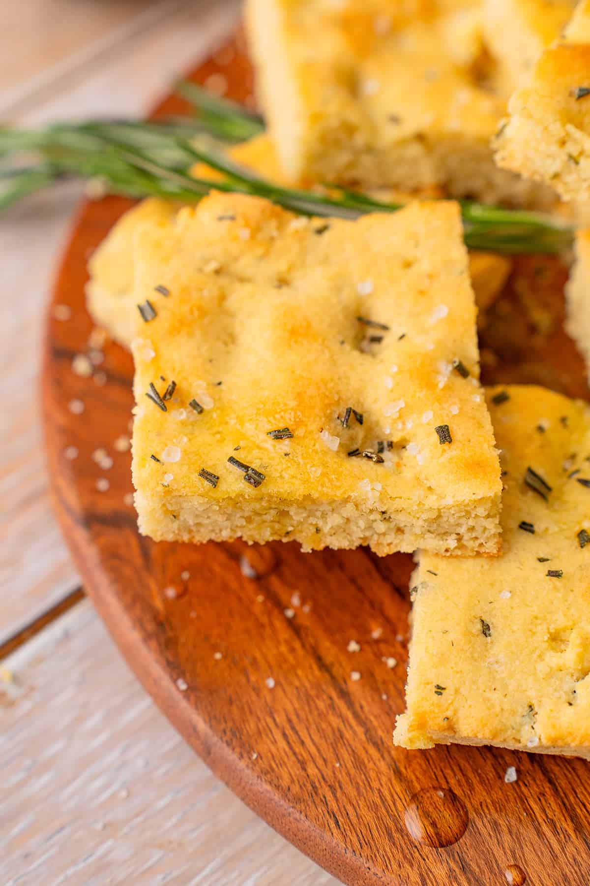Squares of keto focaccia bread on a wooden plate with rosemary.