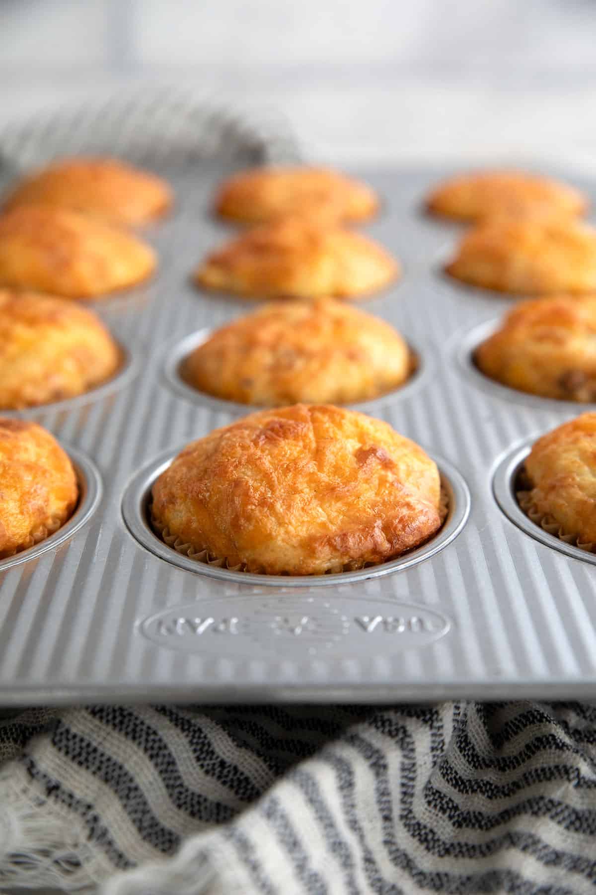 Freshly baked cottage cheese muffins in a metal baking pan over a striped kitchen towel.