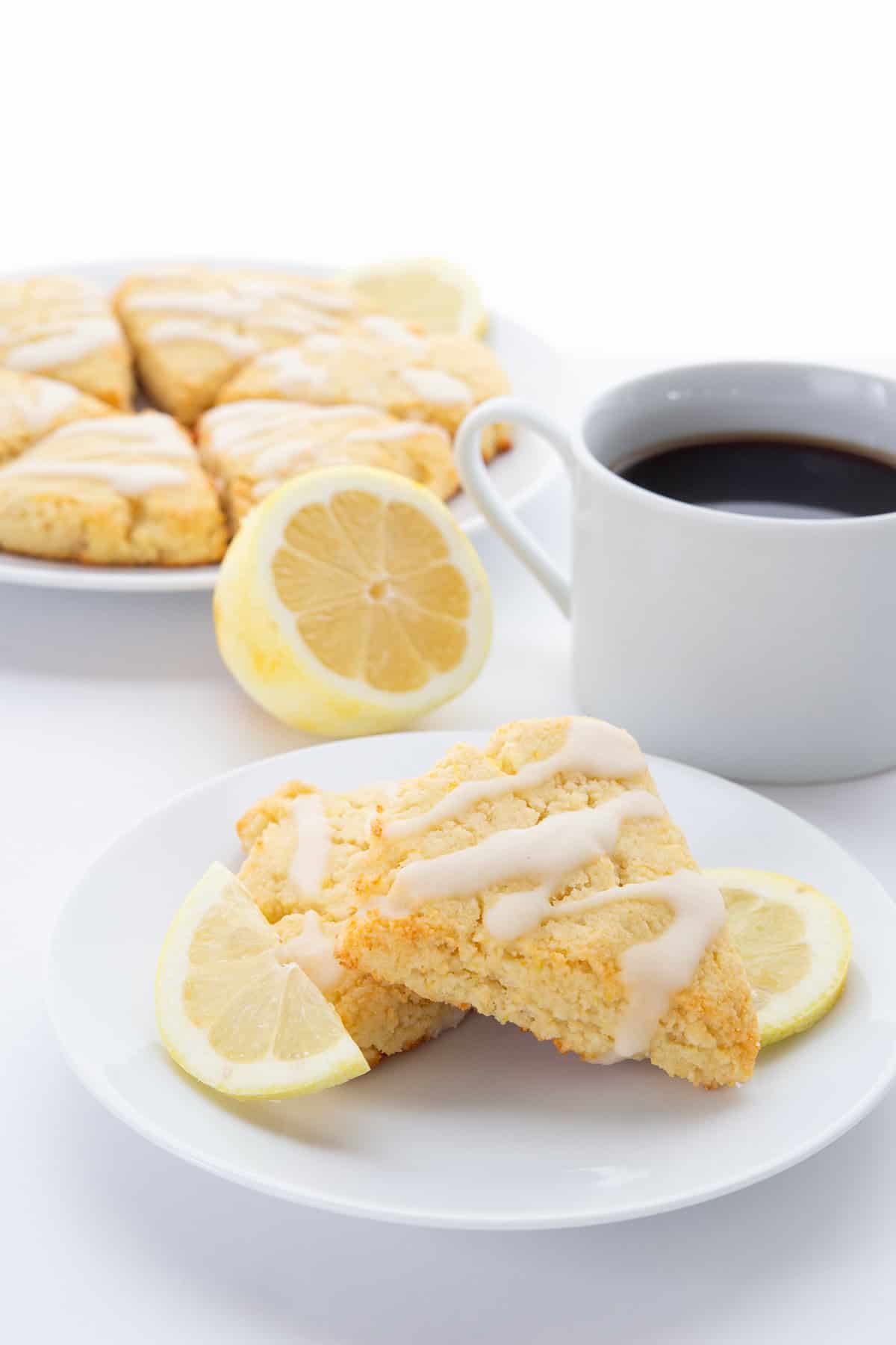 Two Keto Lemon Ricotta Scones on a white plate with a cup of coffee in the background.