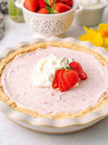 Keto Strawberry Cream Pie in a white pie plate in front of a colander of fresh berries.