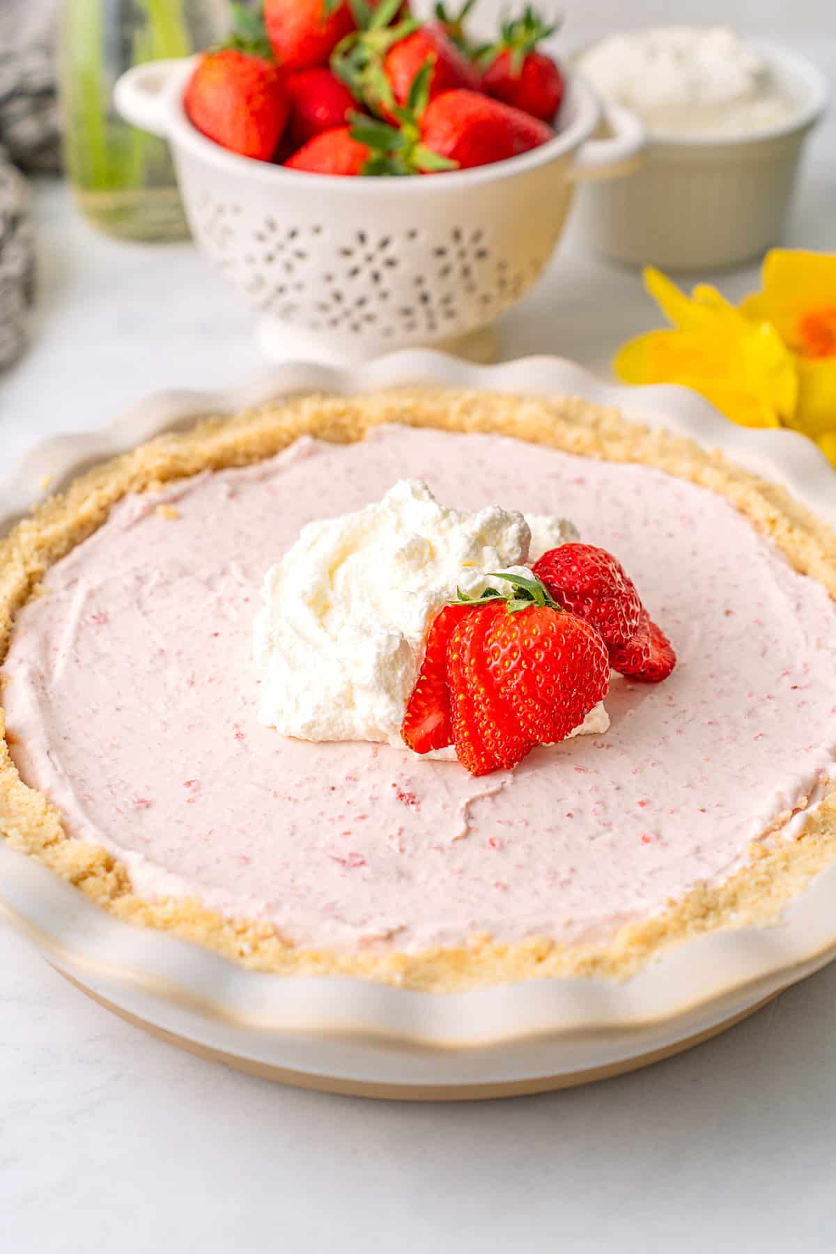 Keto Strawberry Cream Pie in a white pie plate in front of a colander of fresh berries.