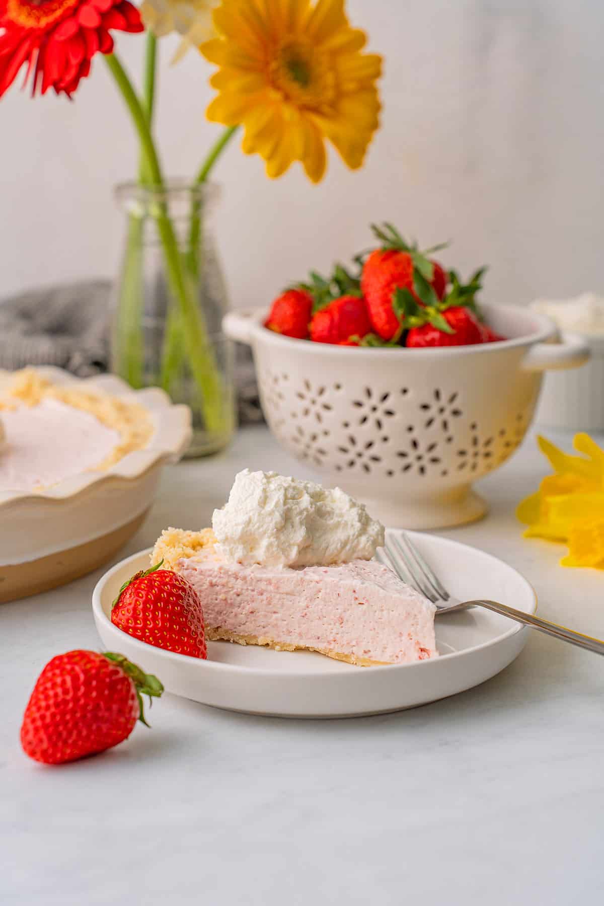 A slice of strawberry cream pie on a white plate on a gray table.