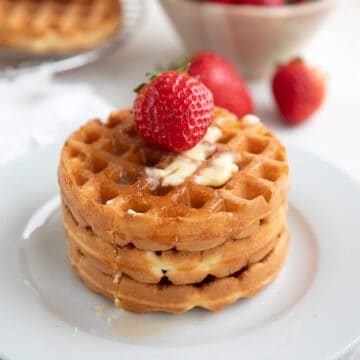 Three keto waffles on a white plate with a strawberry on top.