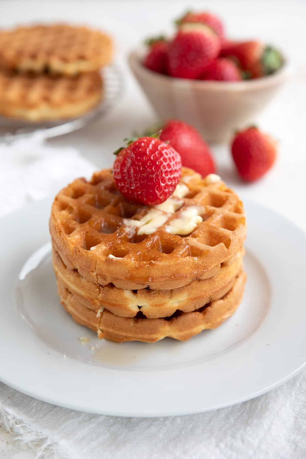 Three keto waffles on a white plate with a strawberry on top.