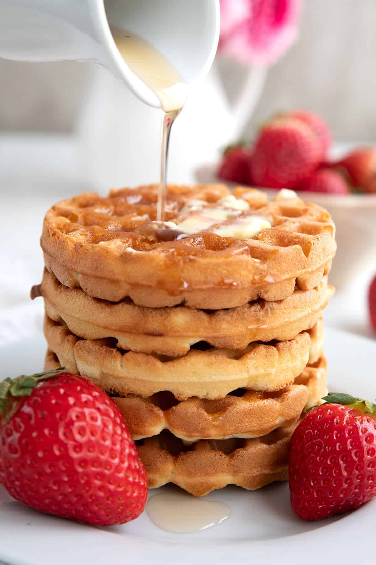 Syrup being drizzled over stack of keto waffles on a white plate with strawberries.