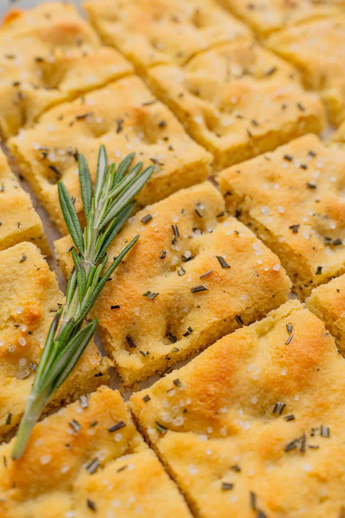 Close up shot of keto focaccia bread cut into squares, with a sprig of rosemary on top.