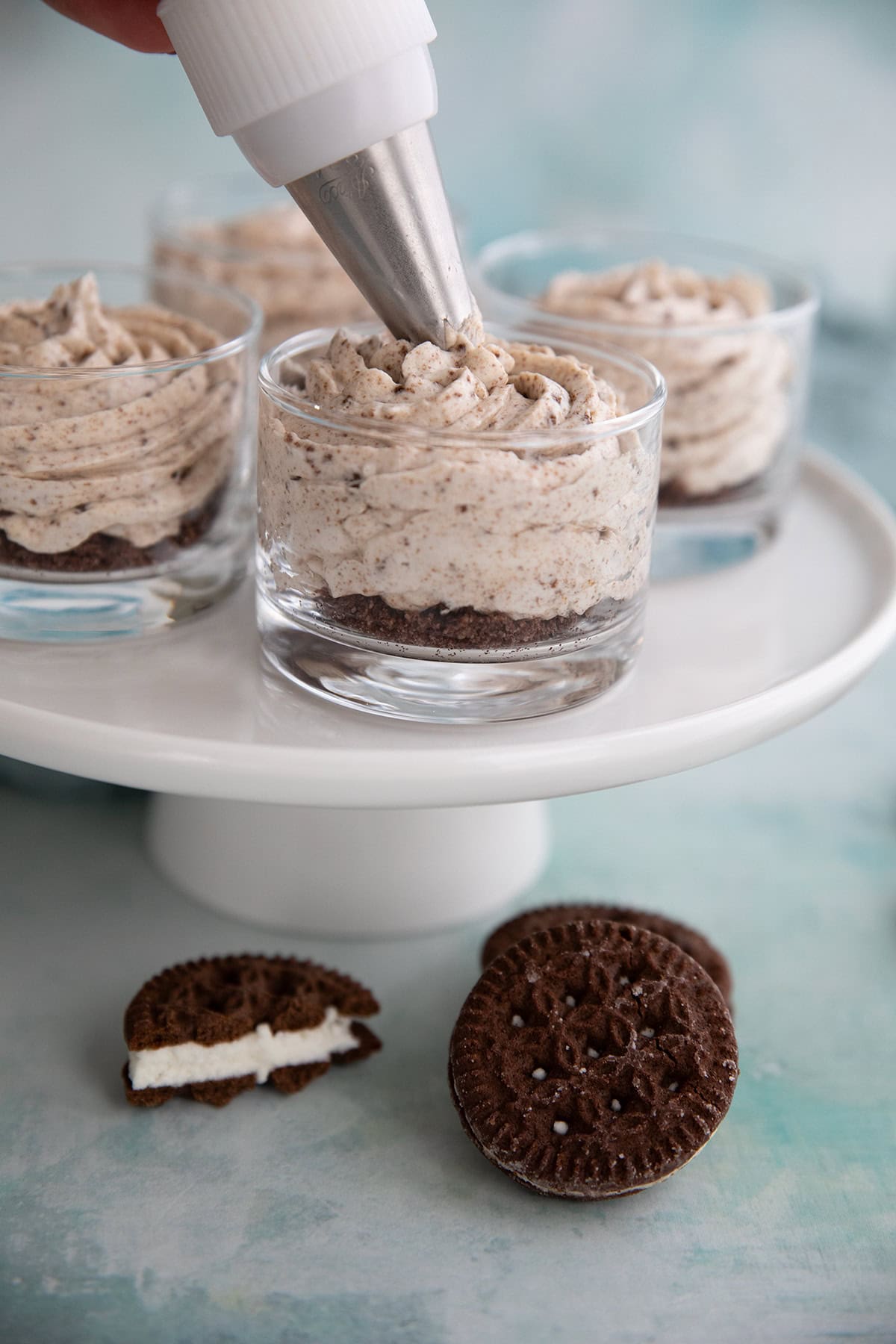 A piping bag piping Keto Cookies and Cream Mousse into glass dessert cups. 