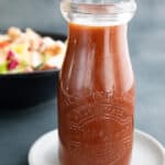 A jar of sugar free French dressing on a white plate, in front of a bowl of salad.