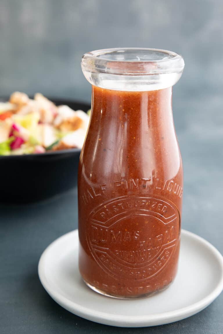 A jar of sugar free French dressing on a white plate, in front of a bowl of salad.