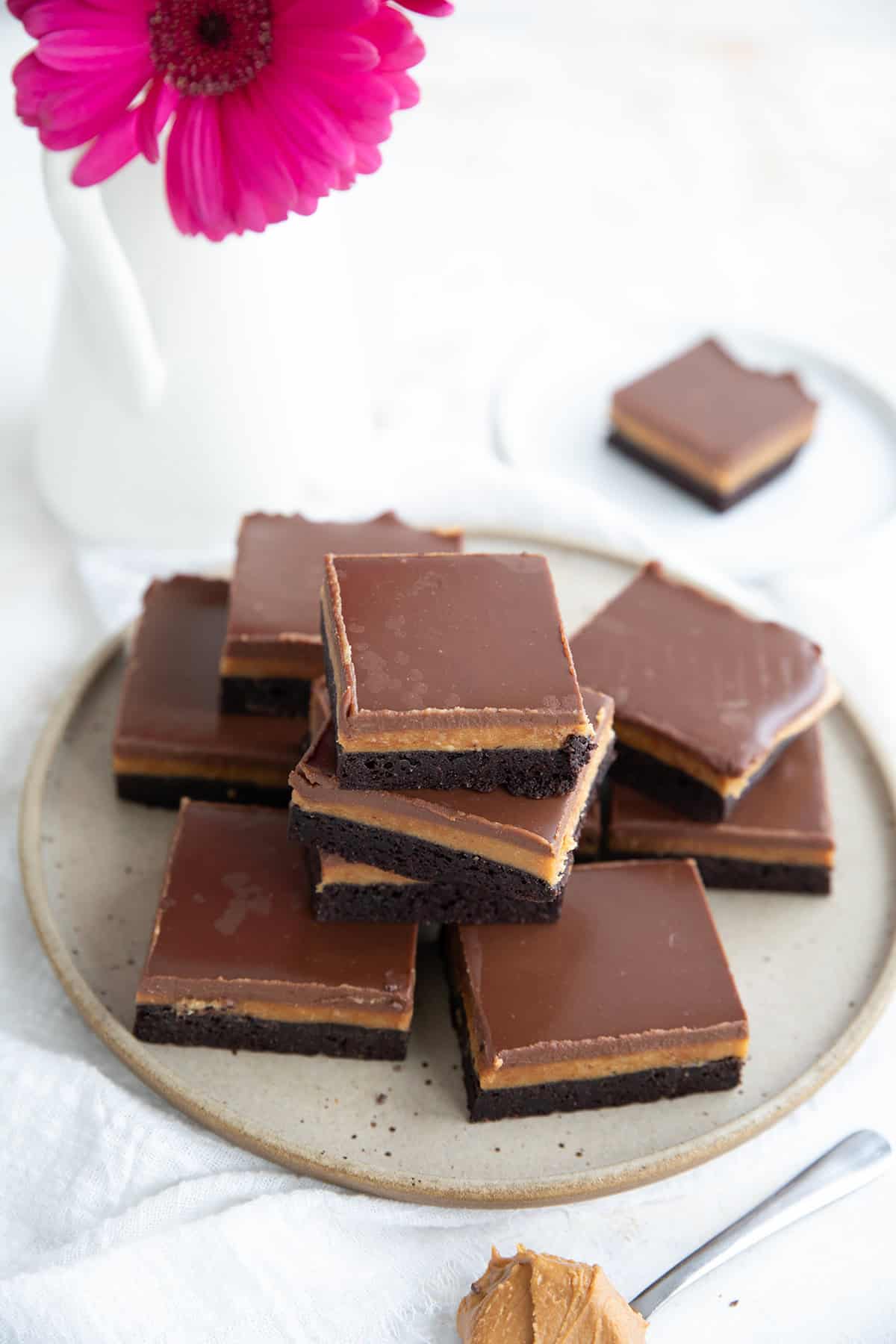 A stack of Buckeye Brownies on a rustic plate with a vase of pink flowers in the background.