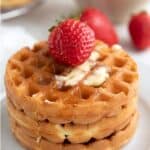 Titled image of a stack of keto waffles on a white plate with a strawberry on top.