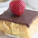 Close up shot of a slice of Keto Boston Cream Poke Cake on a white plate with a strawberry on top.