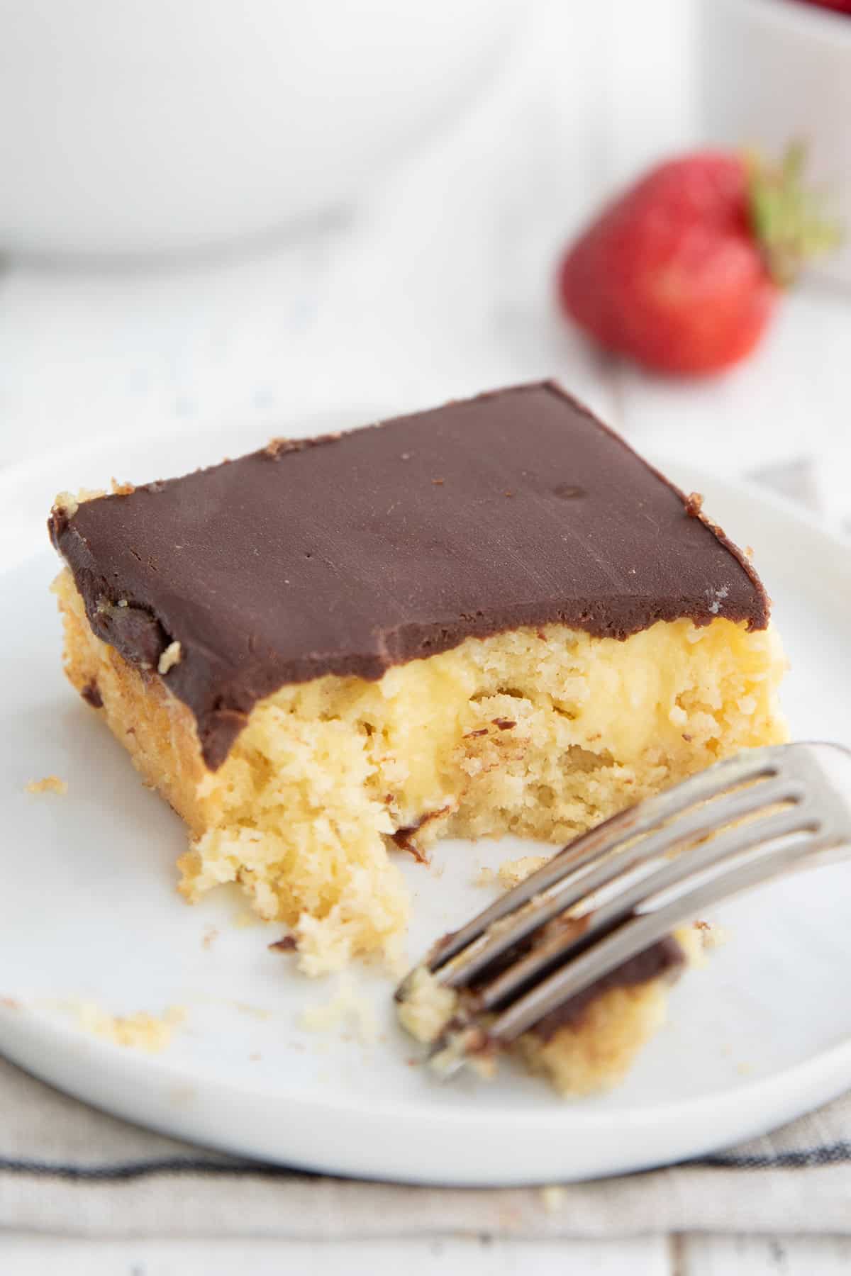 A slice of Keto Boston Cream Poke Cake on a white plate with several forkfuls taken out of it.