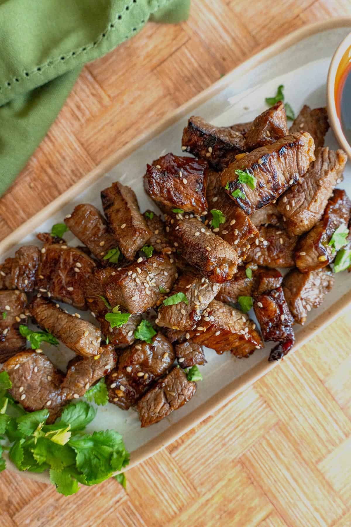 Top down image of Asian Steak Bites on a white platter, on a bamboo table.