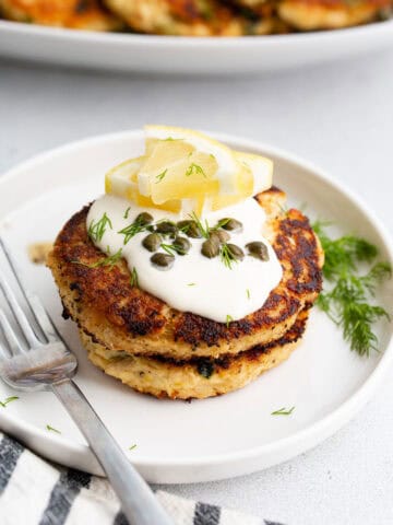 Two tuna patties on a white plate with lemon, dill, and a fork.