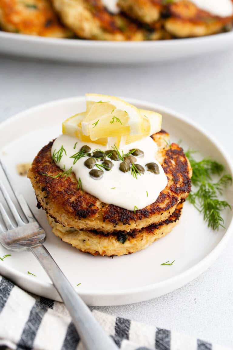 Two tuna patties on a white plate with lemon, dill, and a fork.