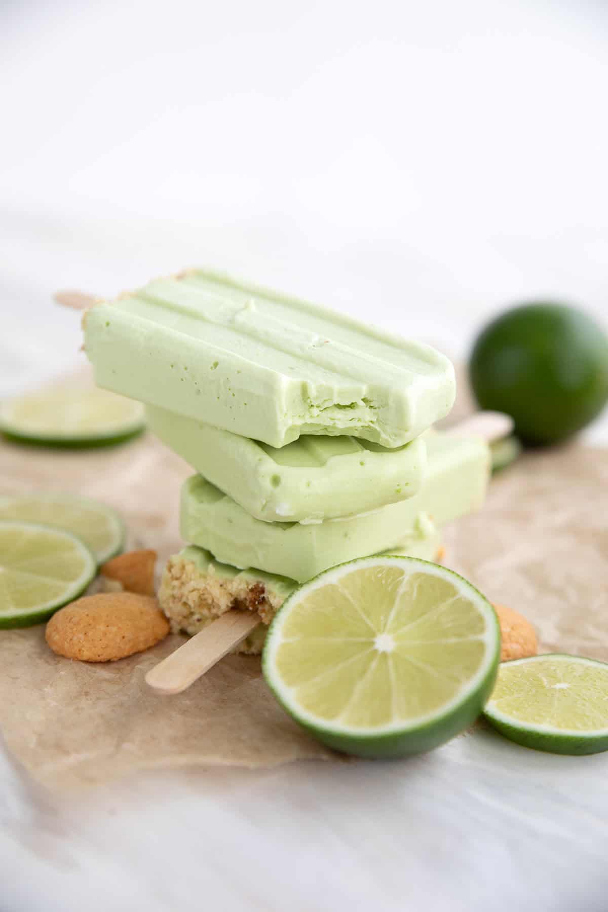 A stack of Keto Key Lime Protein Popsicles surrounded by limes.