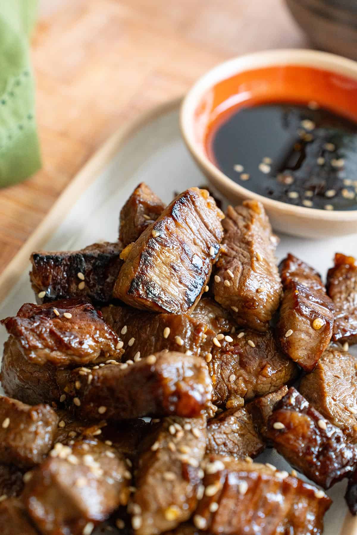 Close up shot of Asian Steak Bites on a white platter with dipping sauce in the background.