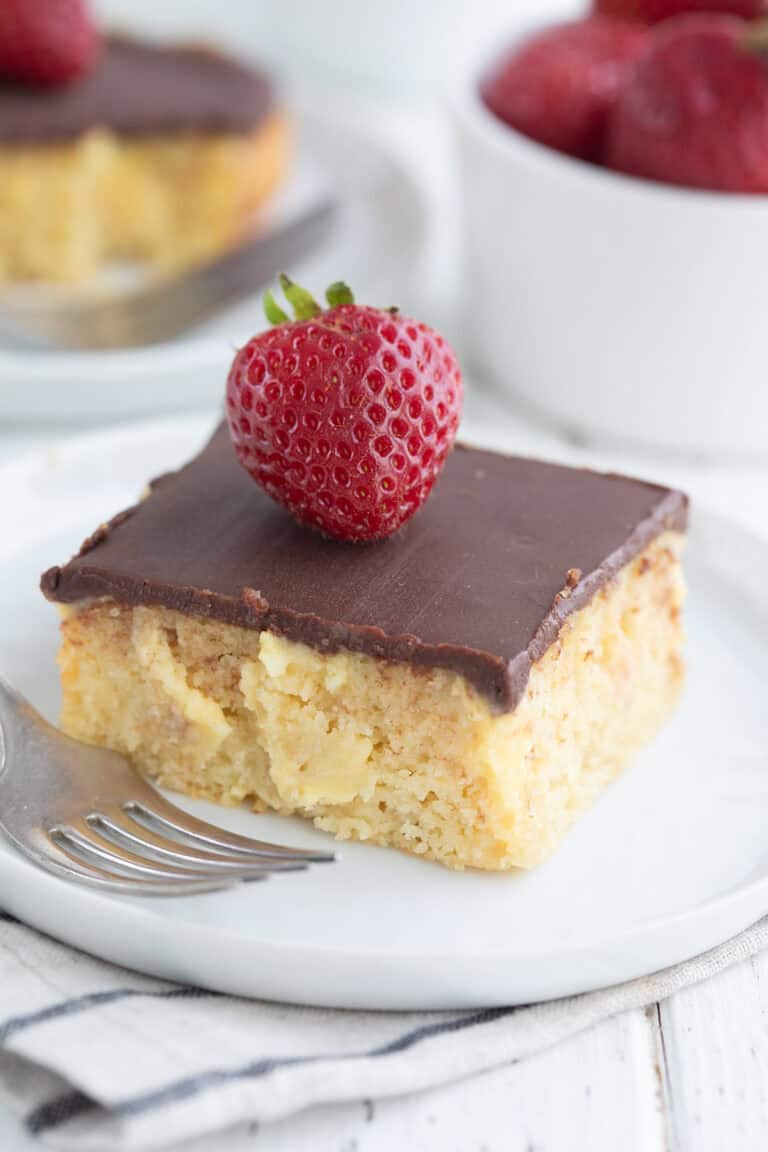 Close up shot of a slice of Keto Boston Cream Poke Cake on a white plate.