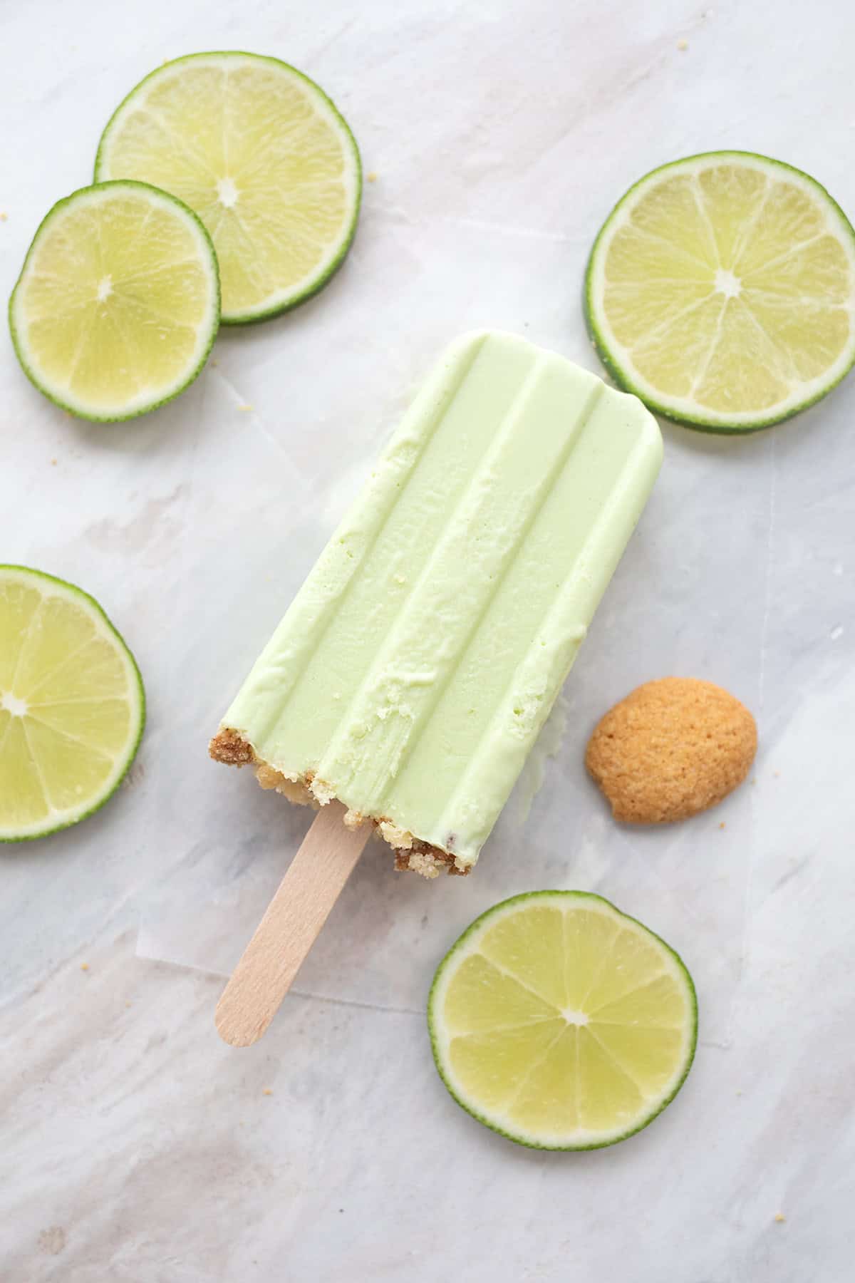 Top down image of a key lime protein popsicles on a marble table with lime slices around it.