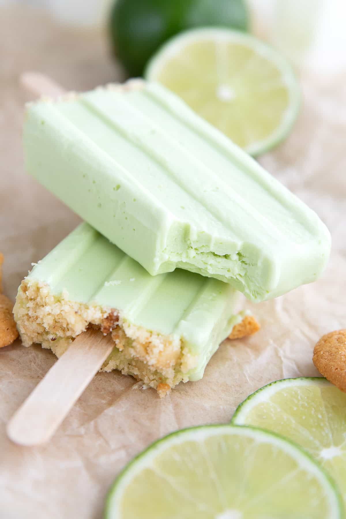 Two keto key lime popsicles on brown paper with a bite taken out of the top one.