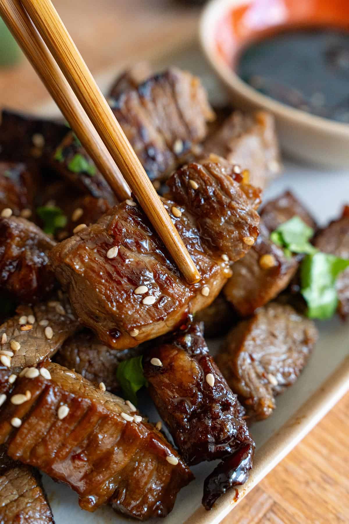 Close up shot of chopsticks picking up some Asian Steak Bites from a plate.