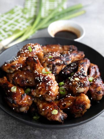 A black bowl filled with Teriyaki Wings on a gray concrete table.
