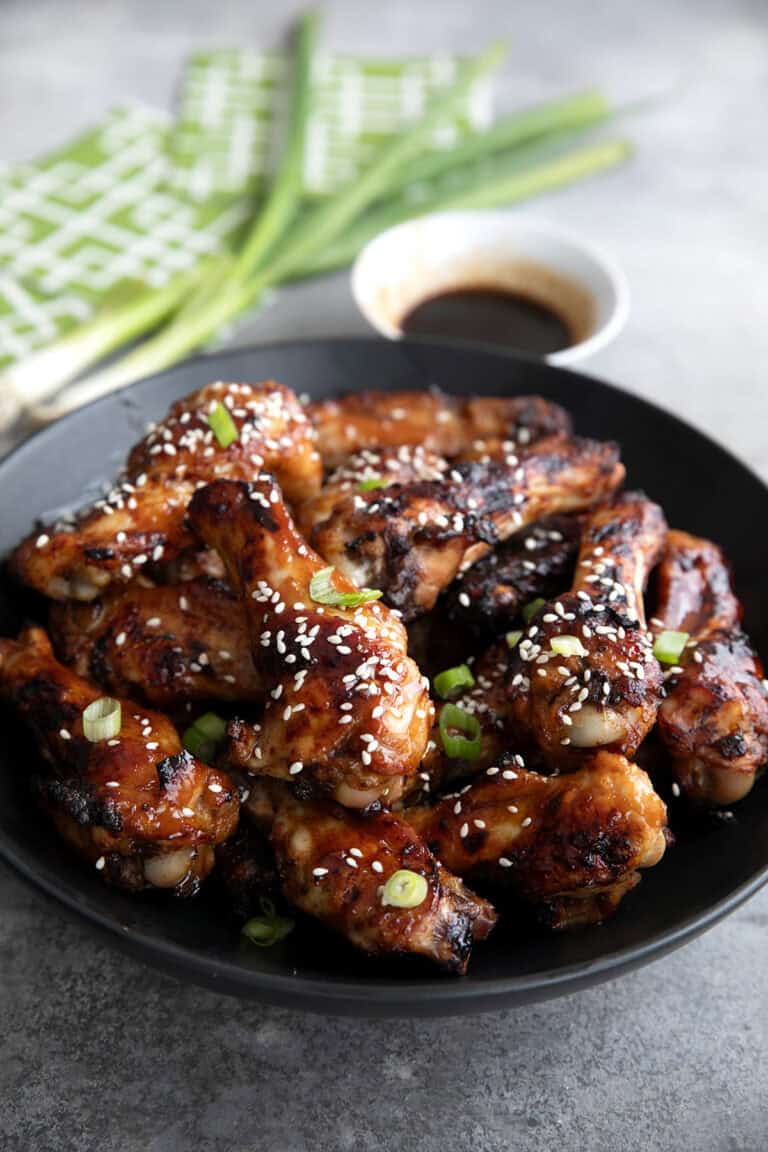 A black bowl filled with Teriyaki Wings on a gray concrete table.