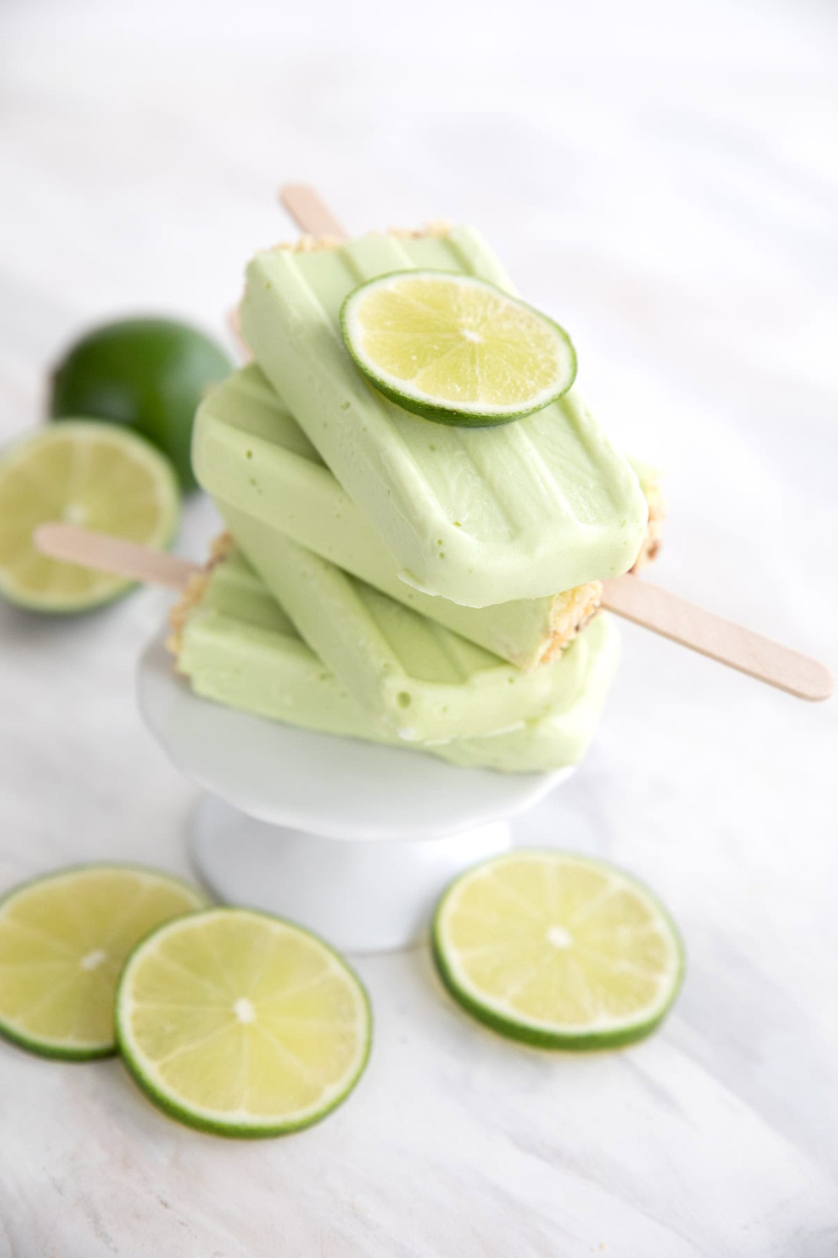 A stack of Key Lime Popsicles on a cake stand with lime slices.